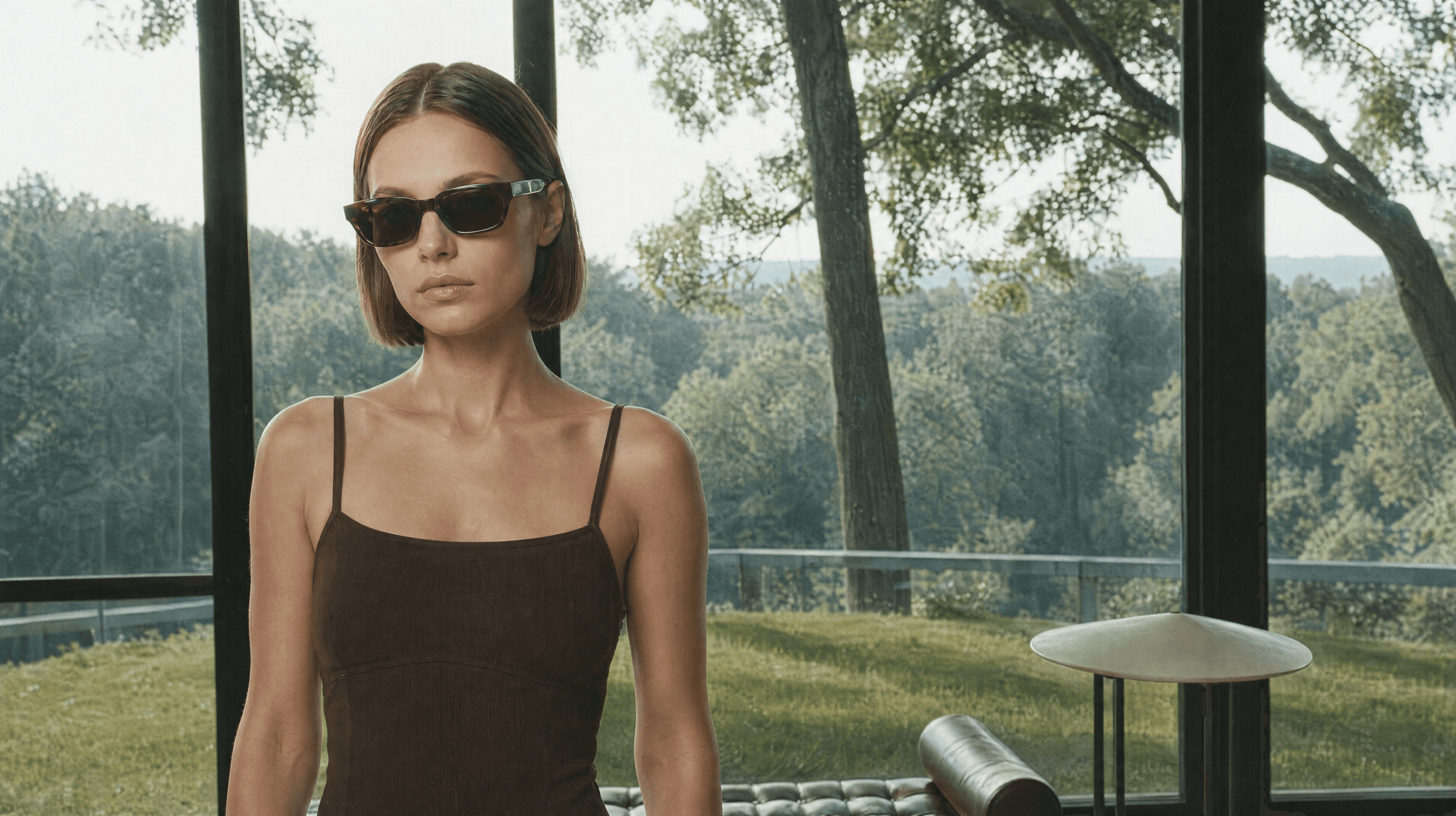 A fashion model standing outdoors in sunglasses against a wooded backdrop.